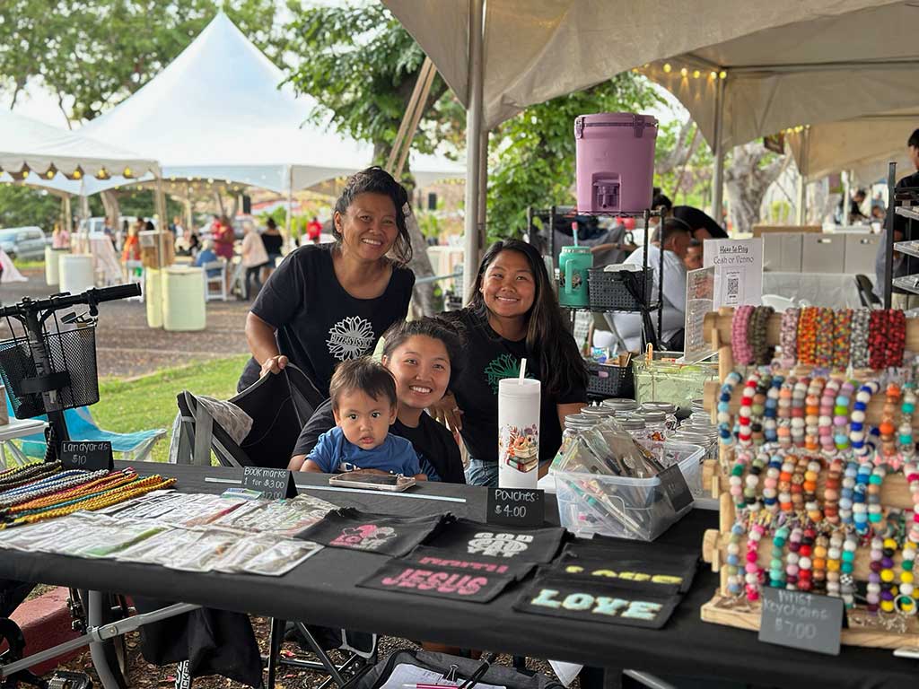 A vendor and her family pose with colorful wrist keychains and other accessories on display at their vendor booth.