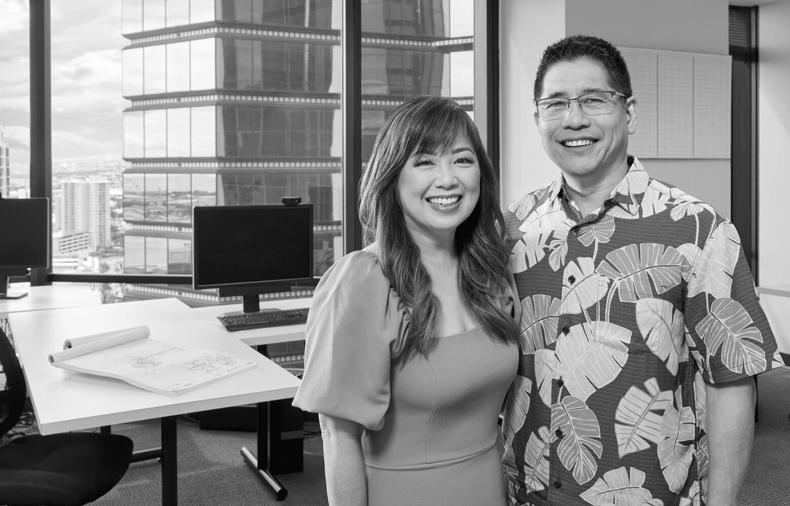 Scott and Joey Inatsuka pose in the Inatsuka Engineering office with the Honolulu skyline behind them.