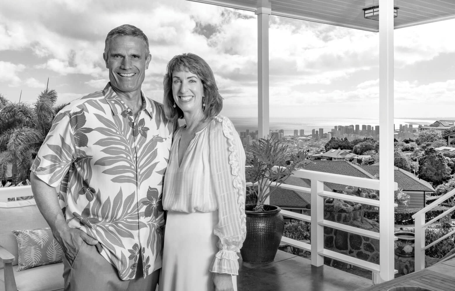 Owners of Nexthome Ku Realty pose on a spacious lanai with a beautiful skyline view in the background.