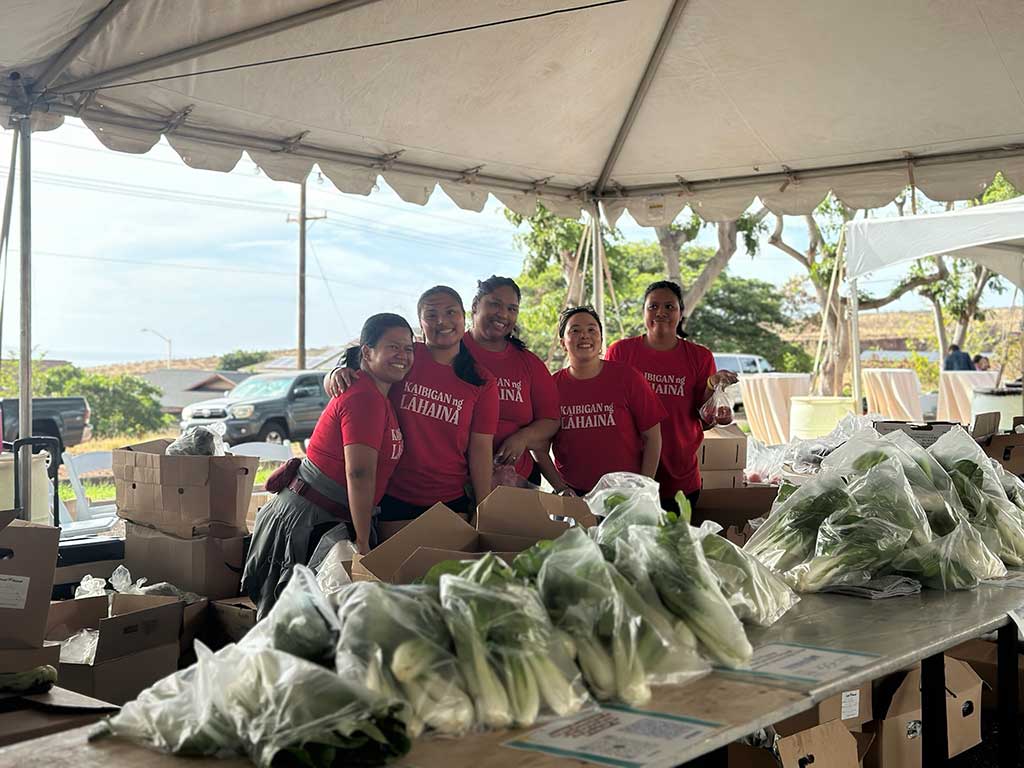 Ladies wearing red Kabigan Ng Lahaina t-shirts display grin as they prepare bags of fresh bok choy for distribution.