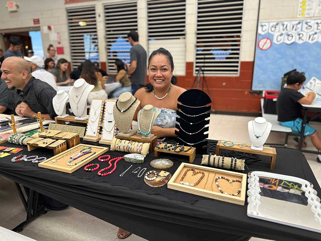 A woman smiles with her handmade jewelry on display.