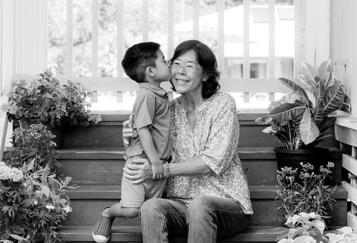 A grandson gives his grandmother a kiss while on the porch steps.