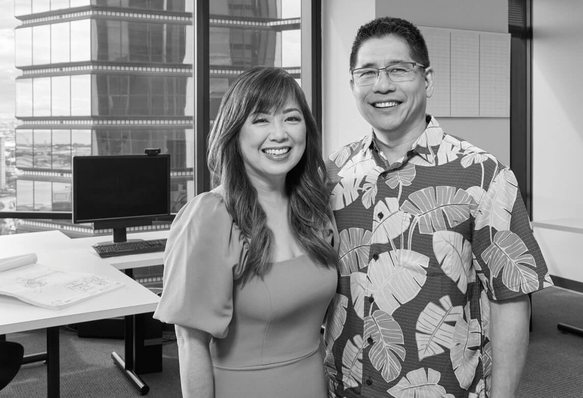 Scott and Joey Inatsuka pose in the Inatsuka Engineering office with the Honolulu skyline behind them.